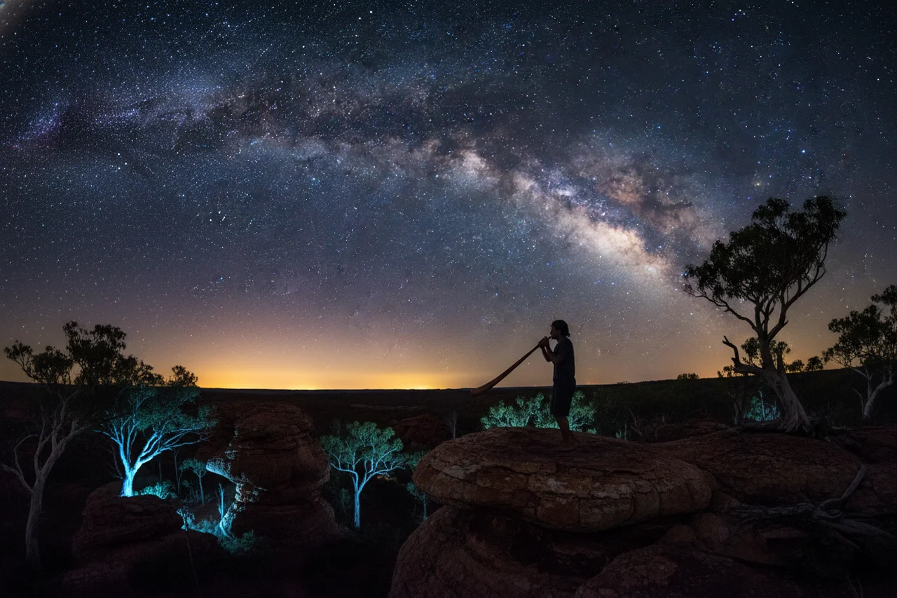 Silueta tocando el didgeridoo bajo la Vía Láctea en un paisaje australiano